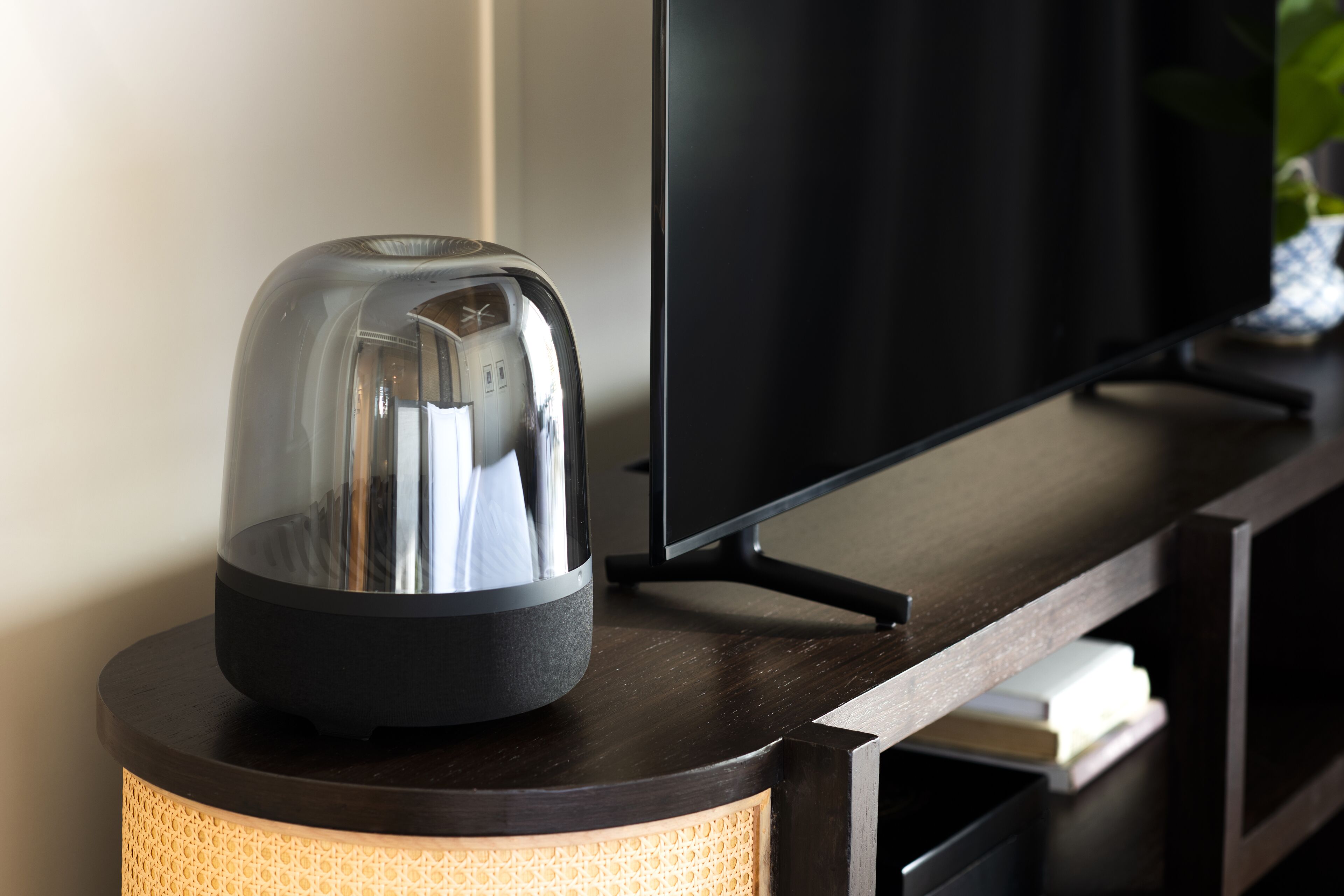 Un salon moderne avec un téléviseur à écran plat, une machine à café posée sur une console en bois et une lampe en osier.