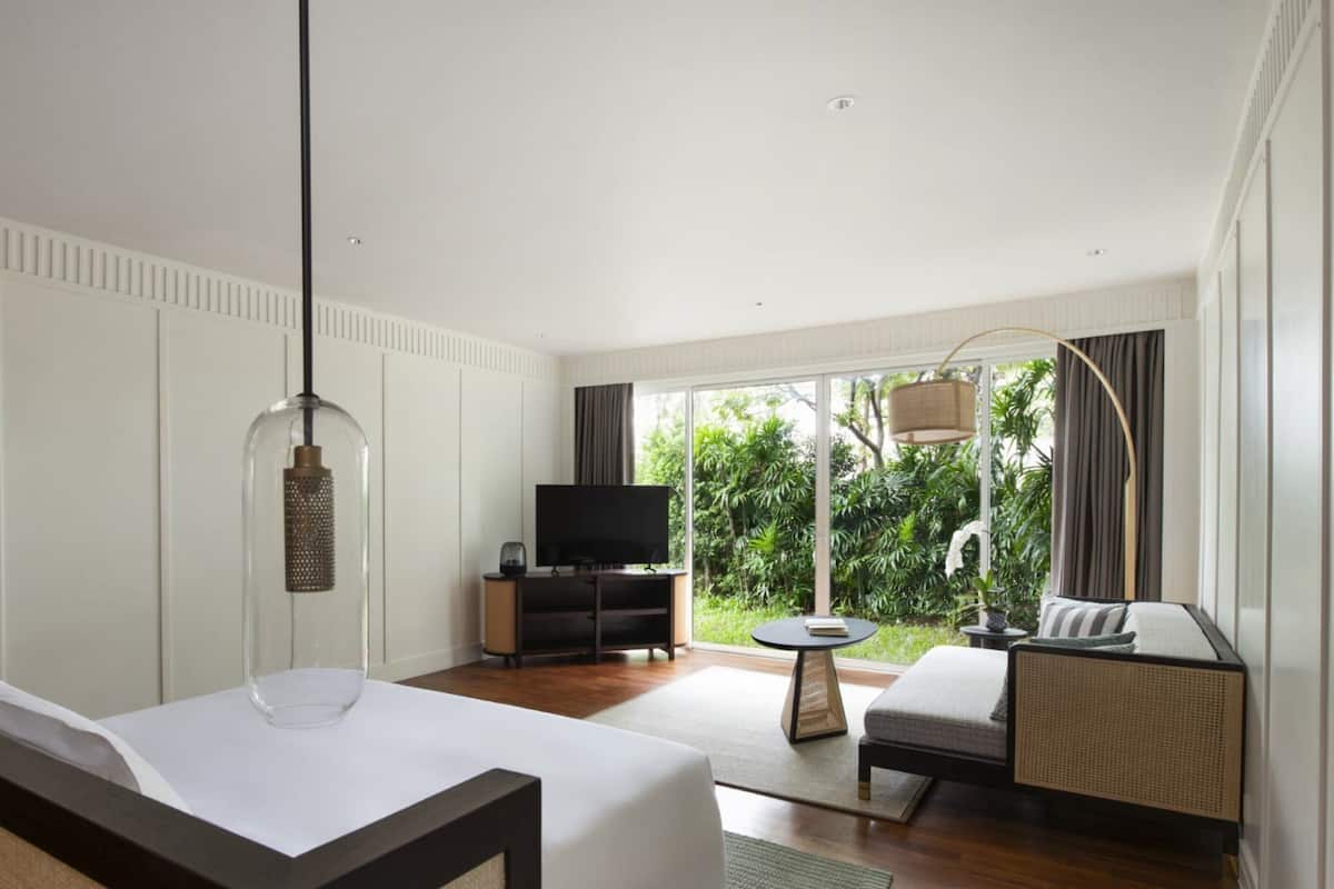 Enjoy a peaceful retreat with a view of lush greenery from the large window, a comfortable seating area, and a flat-screen TV.
