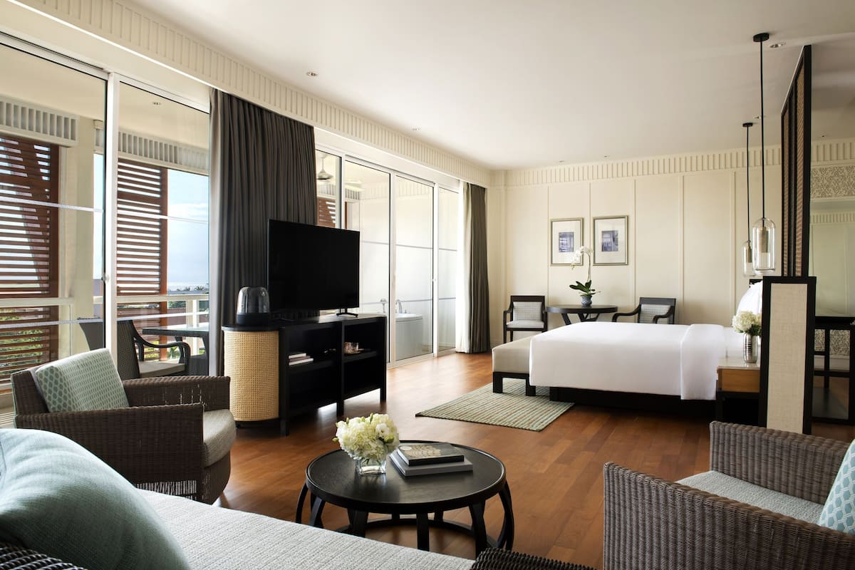 Une chambre d’hôtel moderne dotée d’un grand lit, d’un téléviseur à écran plat, d’un canapé, d’une table basse et d’un coin repas avec une table et des chaises.