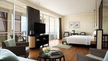 A modern hotel room with a large bed, a flat-screen TV, a sofa, a coffee table, and a dining area with a table and chairs.