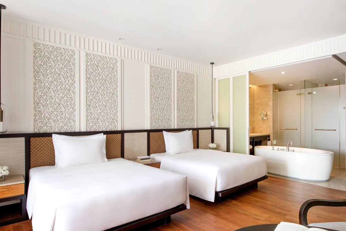 Ett hotellrum med två sängar, ett stort badkar och ett separat badrum med dusch.