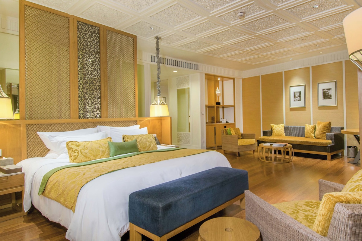 A hotel room with a large bed, a sitting area with a sofa and chairs, a desk, and a bicycle.