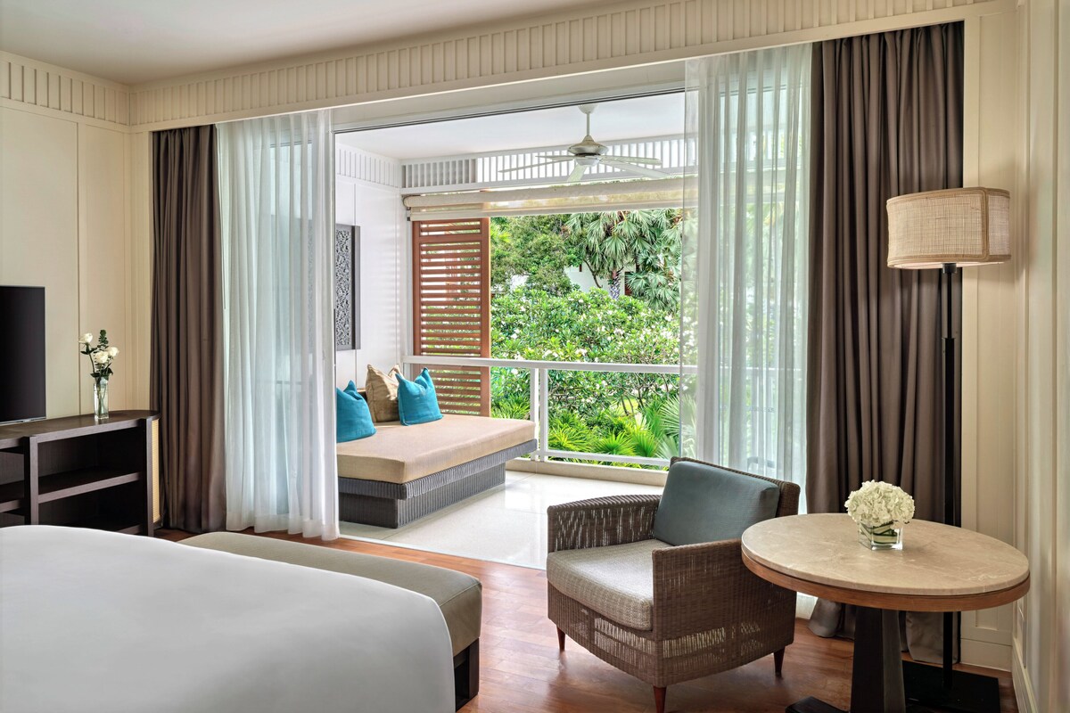 A hotel room with a bed, a sofa, a chair, a small table, and a TV.
