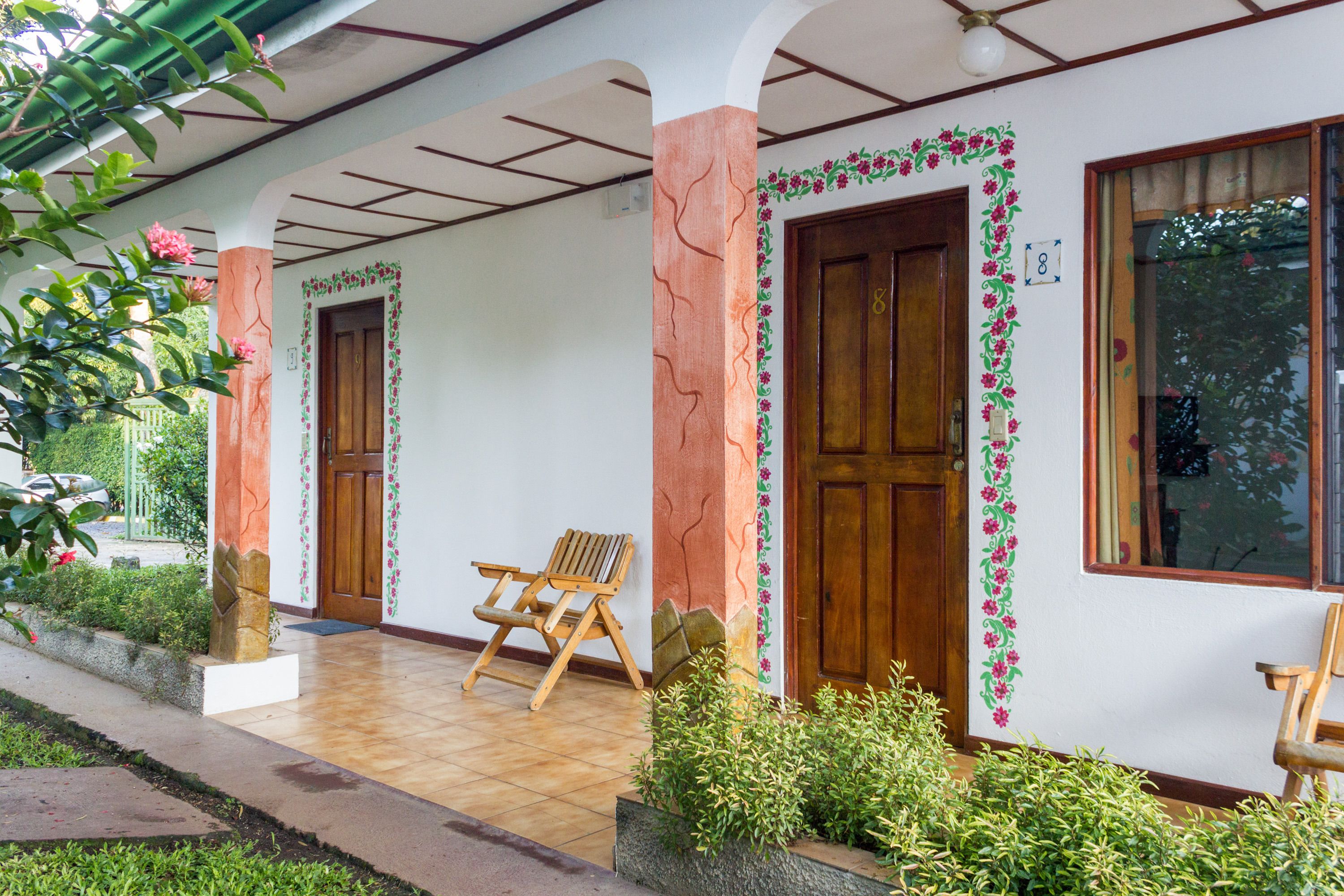Un porche cubierto con puertas de madera, un banco y un pequeño jardín.