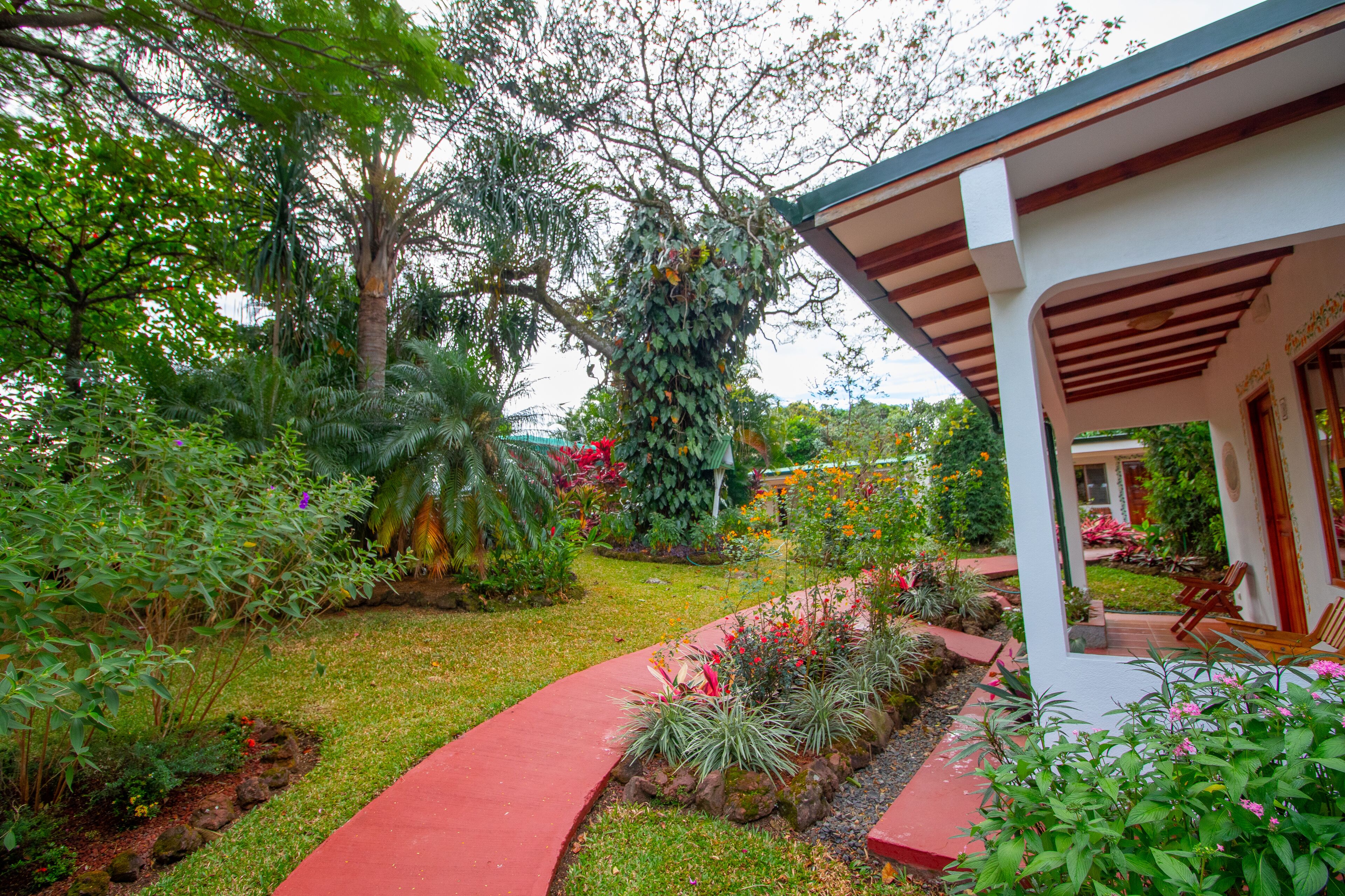 A garden with a curved pathway leading to a covered patio area with chairs.