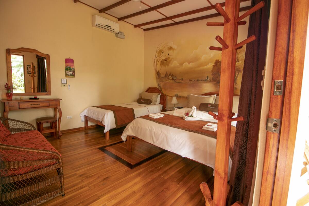 A hotel room with two beds, a wooden desk, a chair, and a large painting on the wall.
