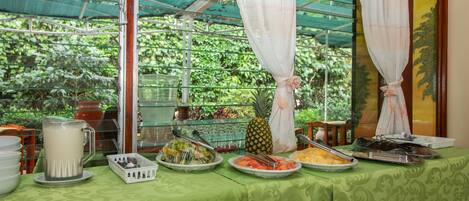 A buffet table with various food items and a pineapple centerpiece, set in a room with a green patterned tablecloth and a glass partition.