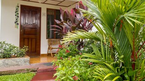 A wooden door, a bench, and a variety of plants including a large palm tree. - Hotel La Rosa de America (San José)