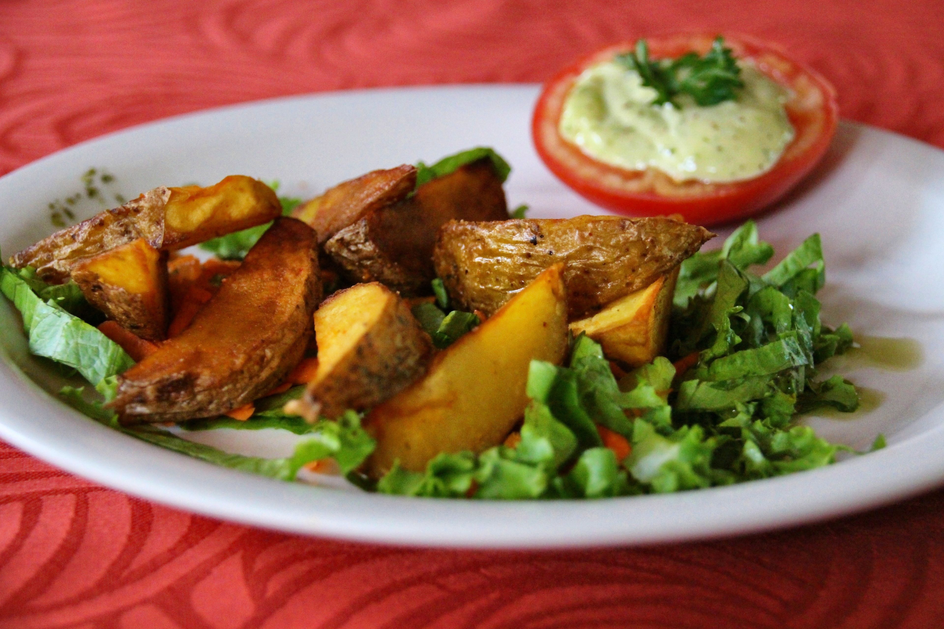 Un piatto con patate arrosto, un pomodoro e verdure a foglia.