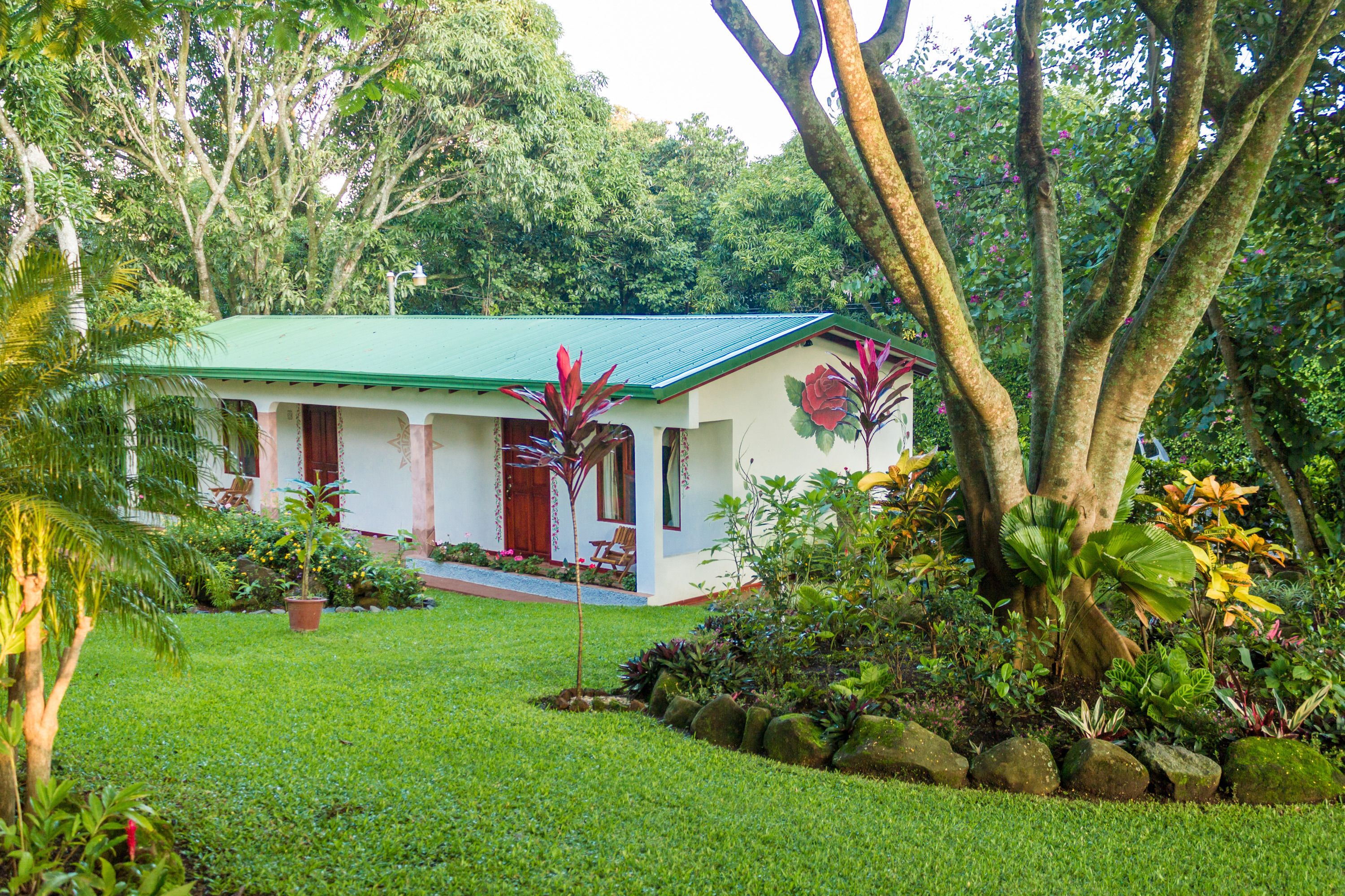 Una casa con techo verde, rodeada de exuberante follaje y plantas tropicales.