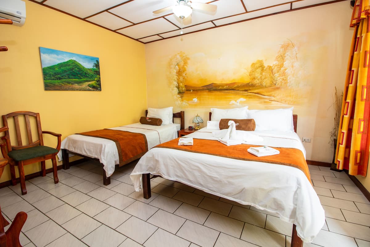 A hotel room with two beds, a painting of a landscape, a ceiling fan, and a window with curtains.