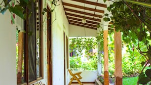 A covered corridor with wooden benches, a tiled floor, and a garden area with plants. - Hotel La Rosa de America (San José)