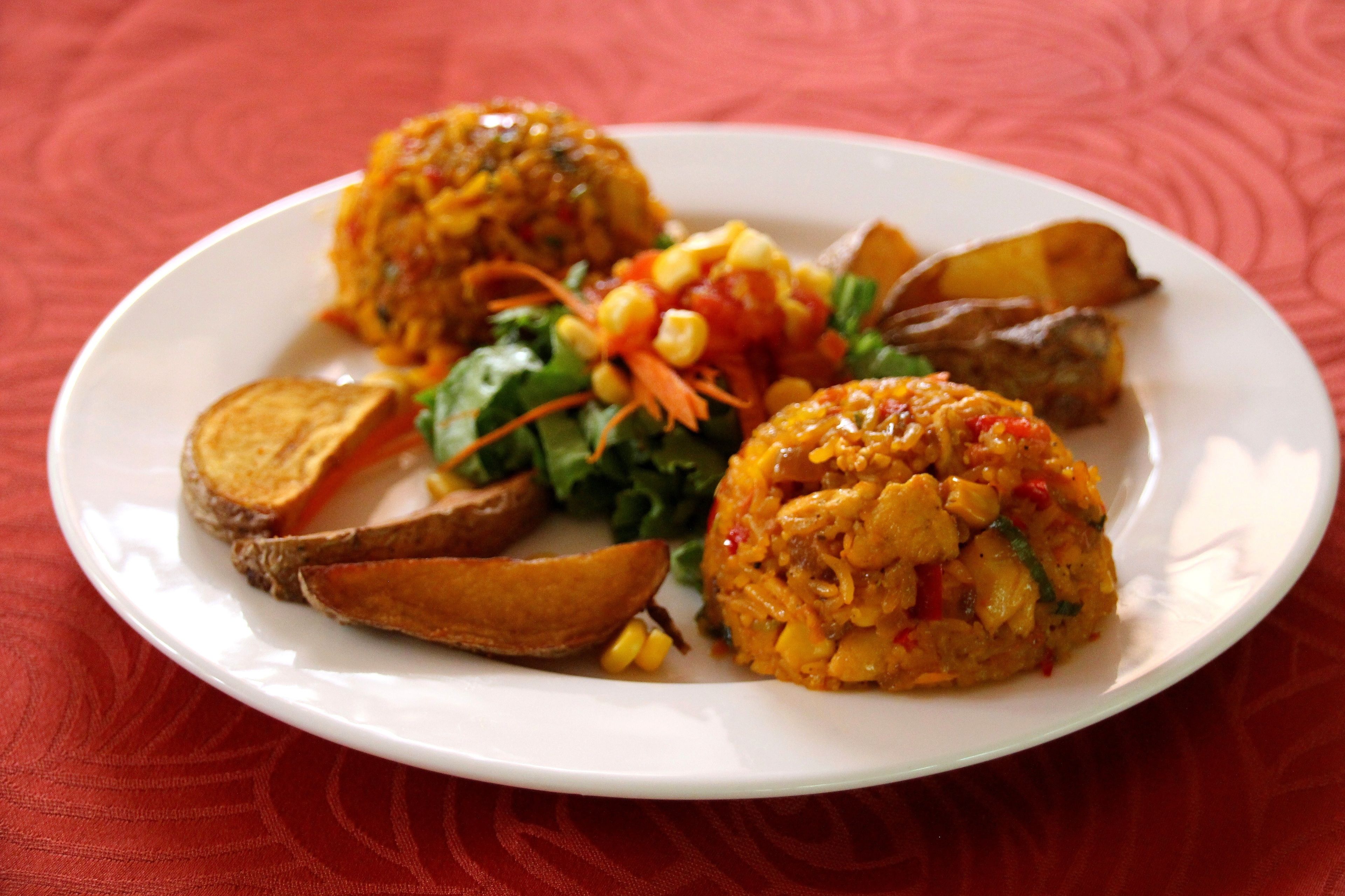 A plate of food with a variety of items including a salad, roasted potatoes, and a rice dish.