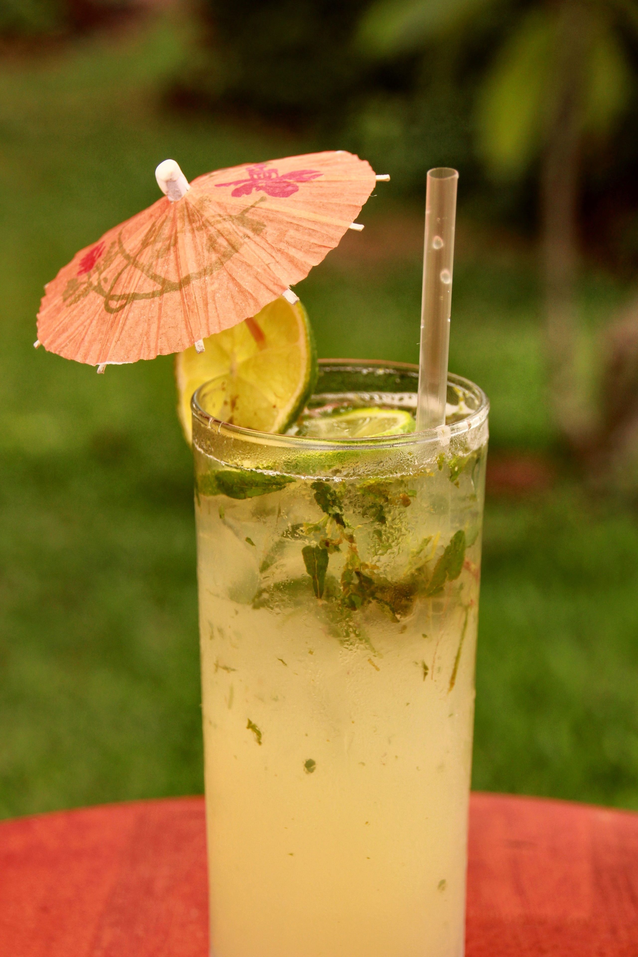 A tall glass with a lime slice and mint garnish, a straw, and a decorative umbrella on top.