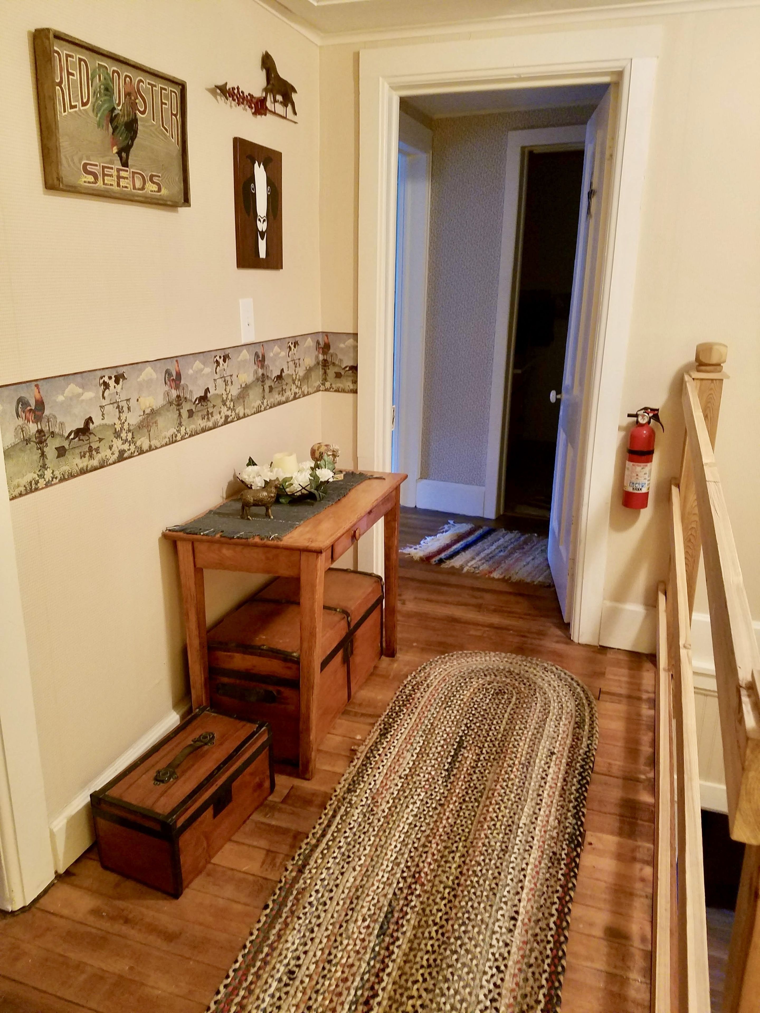 Un pasillo con un banco de madera, un tapete, un cartel en la pared y un extintor.
