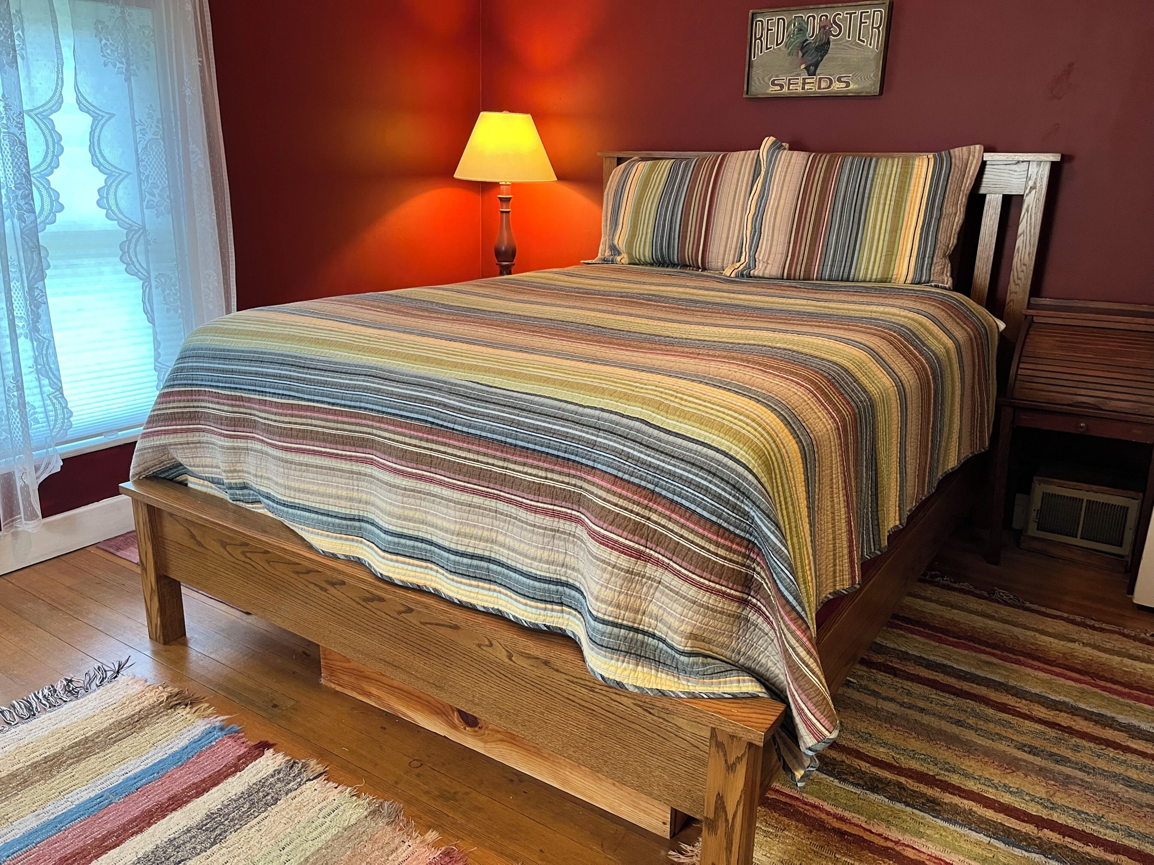 A bed with a striped bedspread, a wooden headboard, a lamp, and a wall with a sign.
