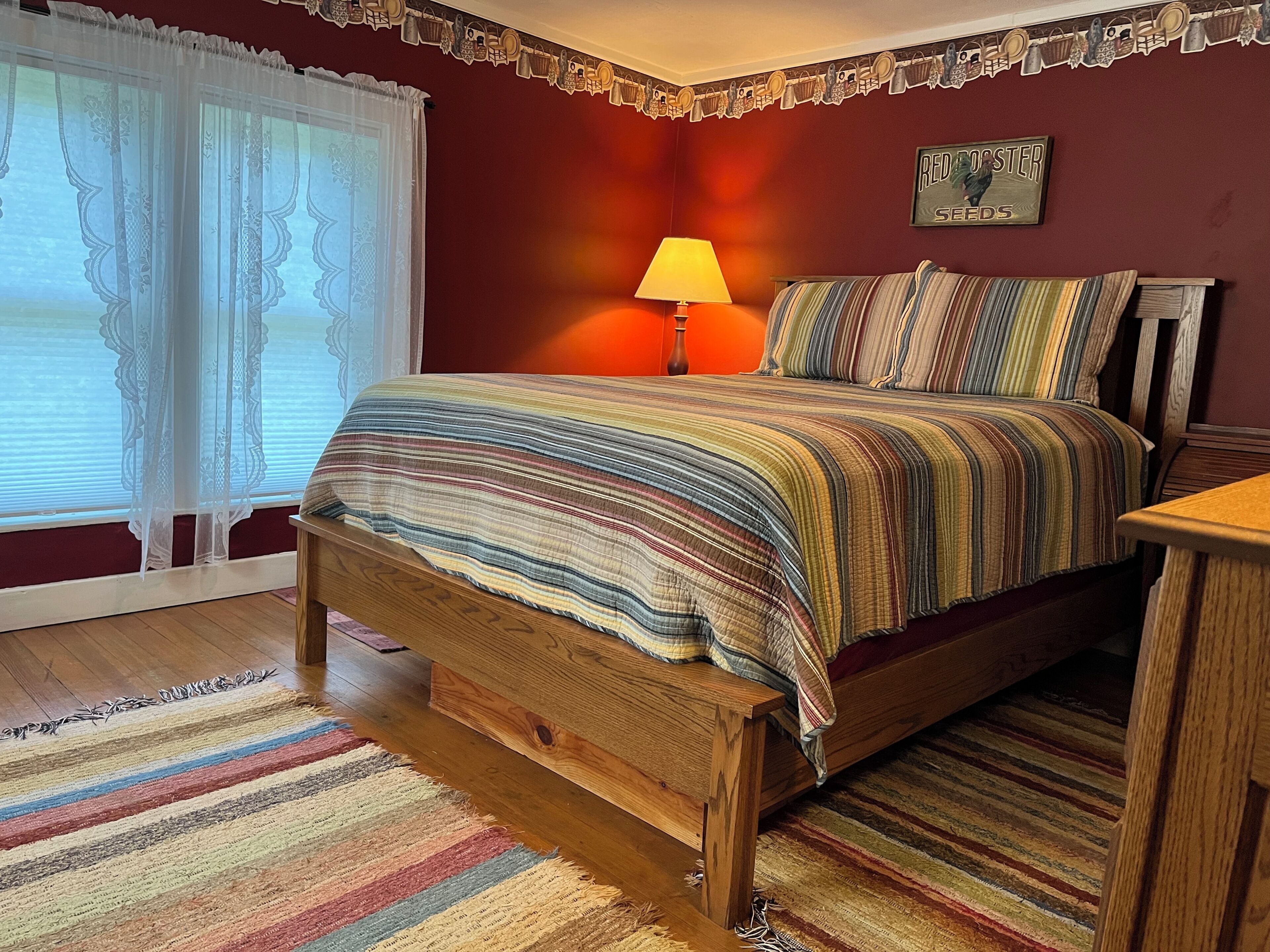 A bedroom with a wooden bed, a bedside table, a lamp, and a window with curtains.