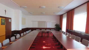 Une salle de conférence avec de longues tables, des chaises, un crucifix au mur et une plante.