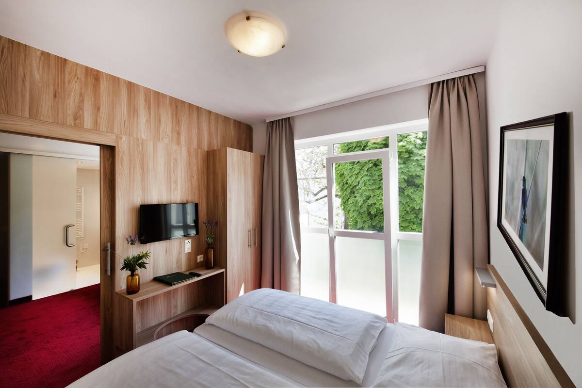 Une chambre d’hôtel avec un lit, une télévision, un bureau agrémenté d’une plante et une fenêtre avec des rideaux.