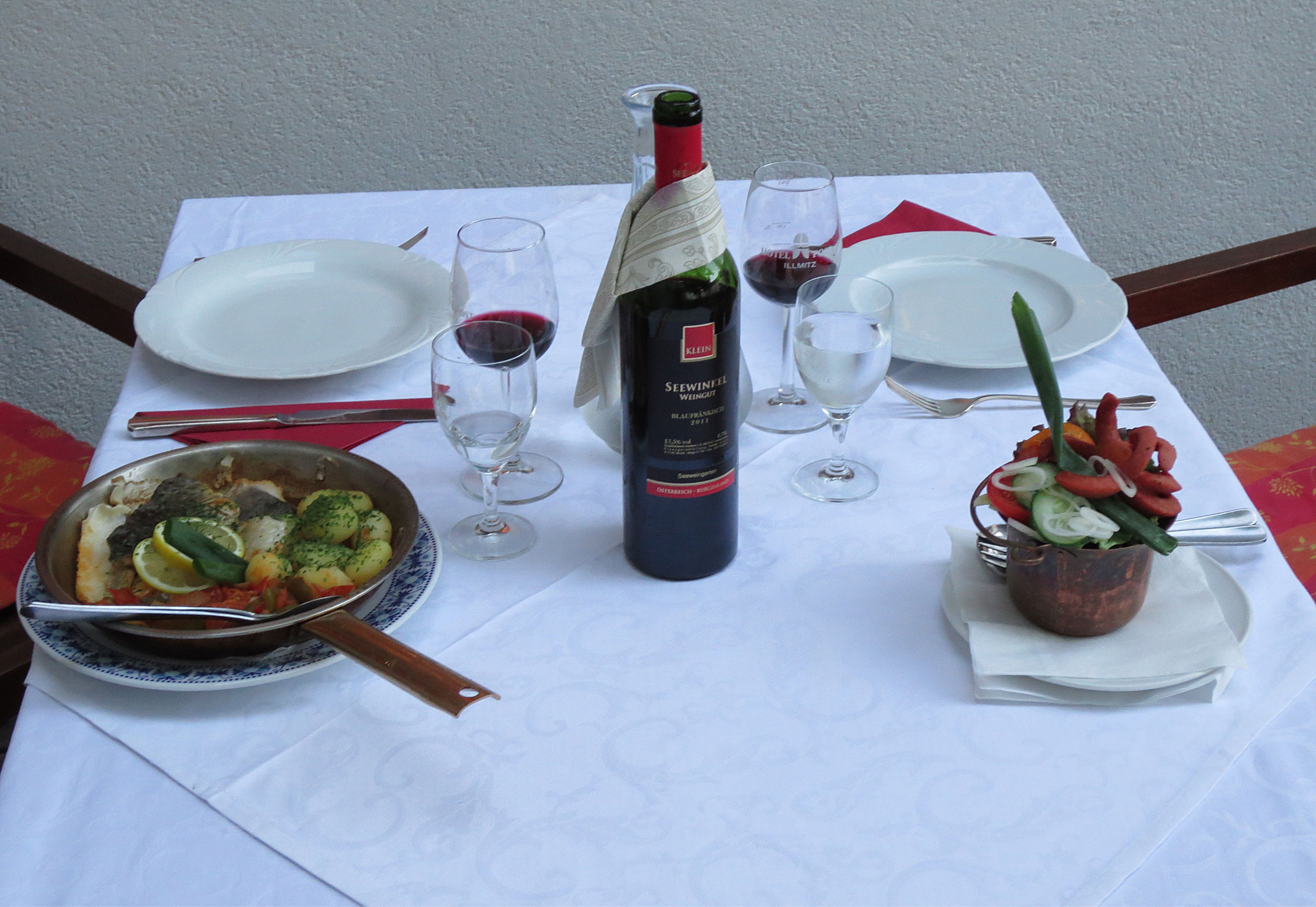 Una mesa puesta para una comida, con platos, vasos, cubiertos, una botella de vino y un bol de verduras.
