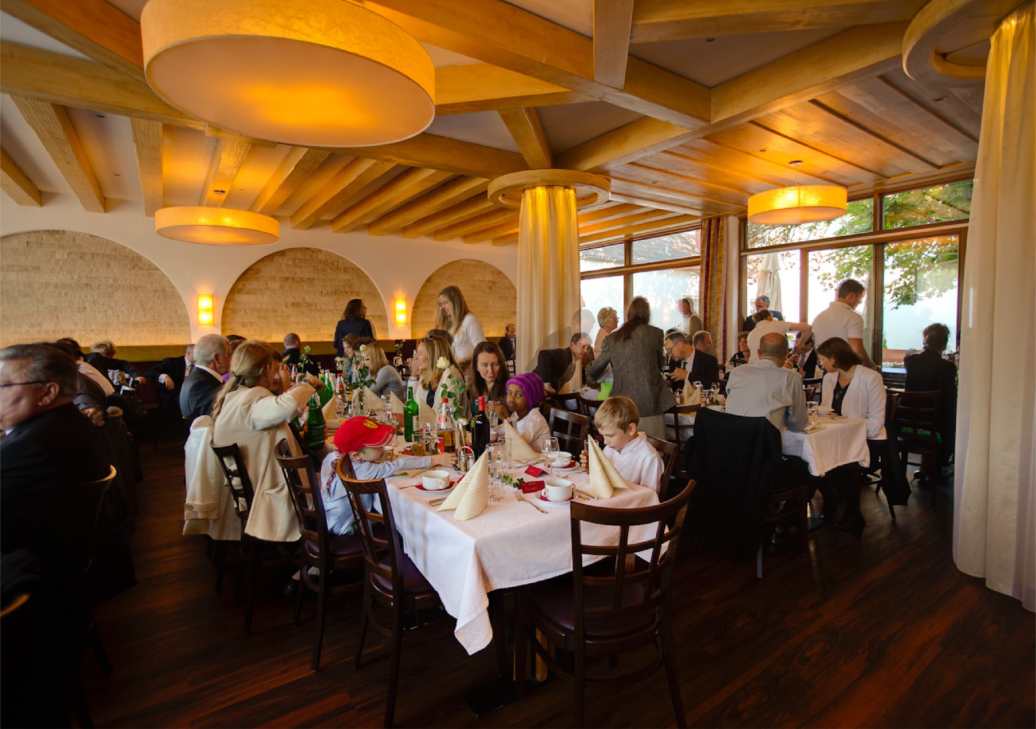 Un restaurante con vigas de madera y ventanas amplias, mesas dispuestas con manteles blancos y diversos platos.