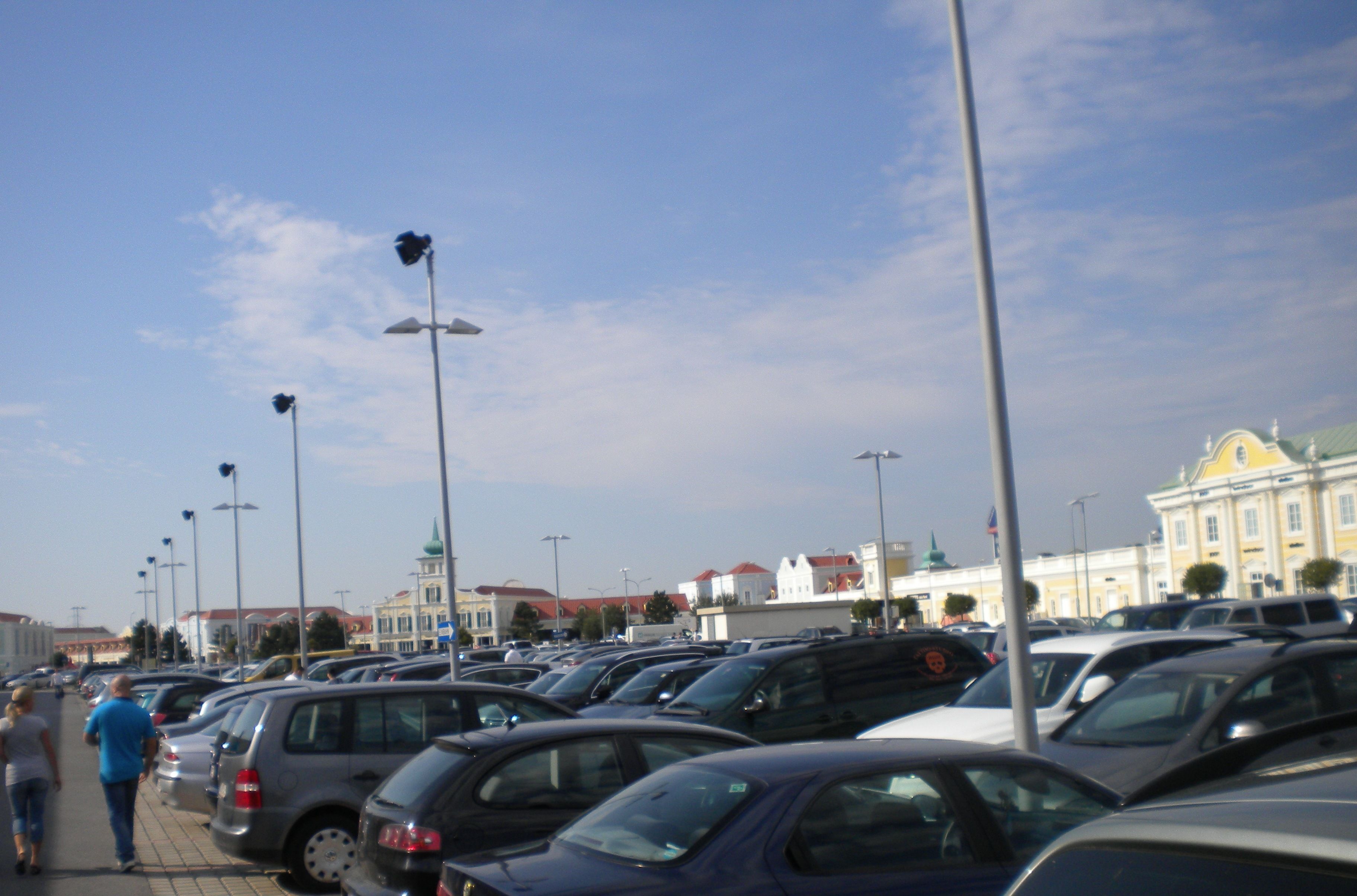 A parking lot with multiple cars and a few pedestrians walking.