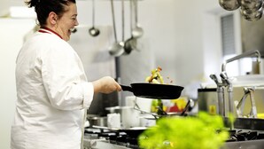 Un chef, vêtu d’un uniforme blanc, cuisine dans une cuisine professionnelle équipée d’appareils en acier inoxydable et d’ustensiles suspendus.
