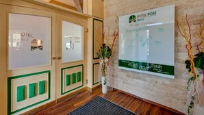 Un espace d’accueil d’hôtel comprenant des meubles de rangement en bois, un comptoir de réception et un panneau mural indiquant le nom de l’hôtel et les services qu’il propose.