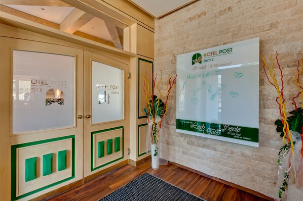 A hotel reception area with wooden cabinets, a reception desk, and a wall-mounted sign with the hotel's name and services.
