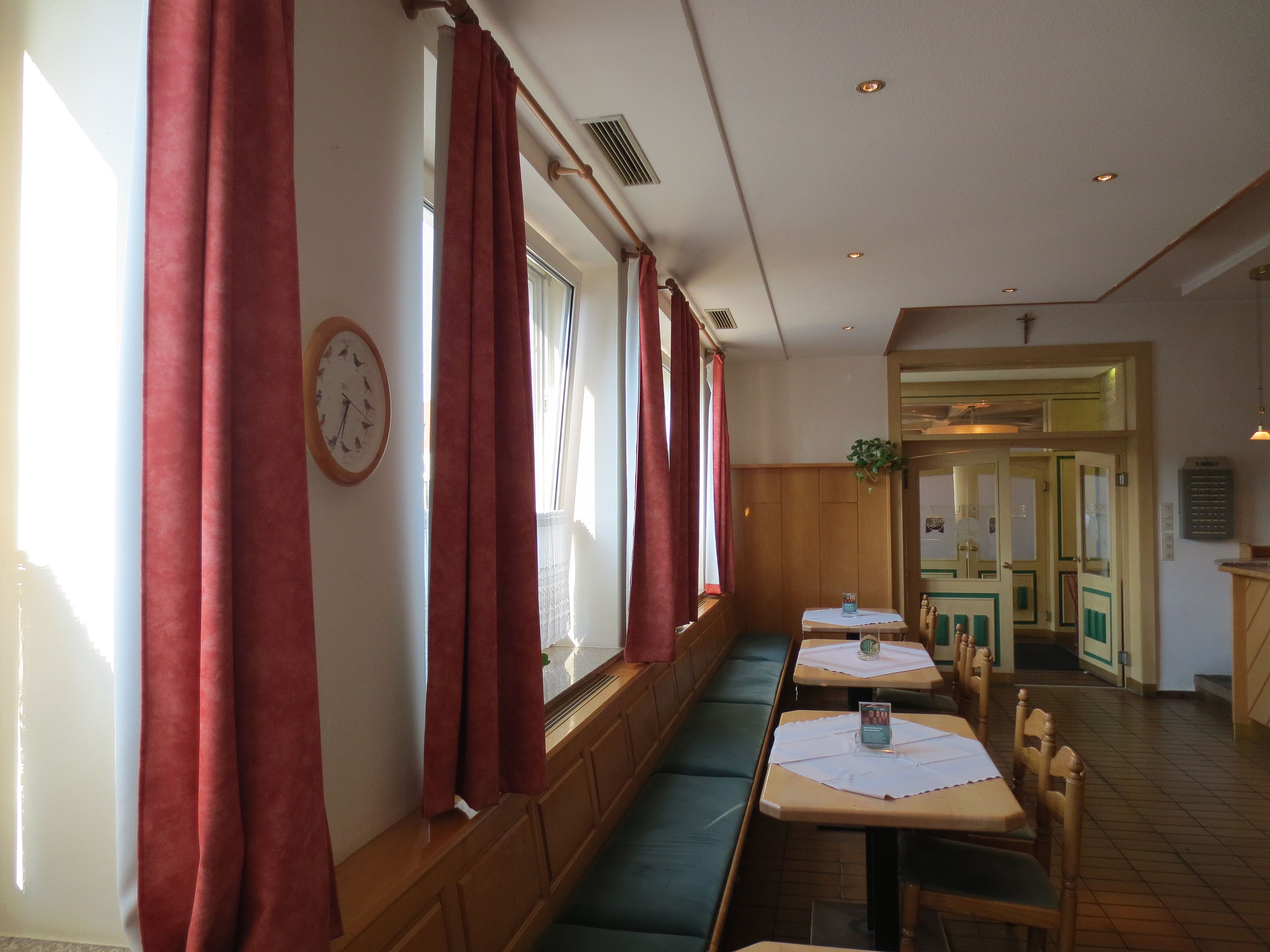 Un restaurante con cabinas y mesas, cortinas rojas, un reloj y una planta.