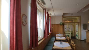 Un restaurante con cabinas y mesas, cortinas rojas, un reloj y una planta.
