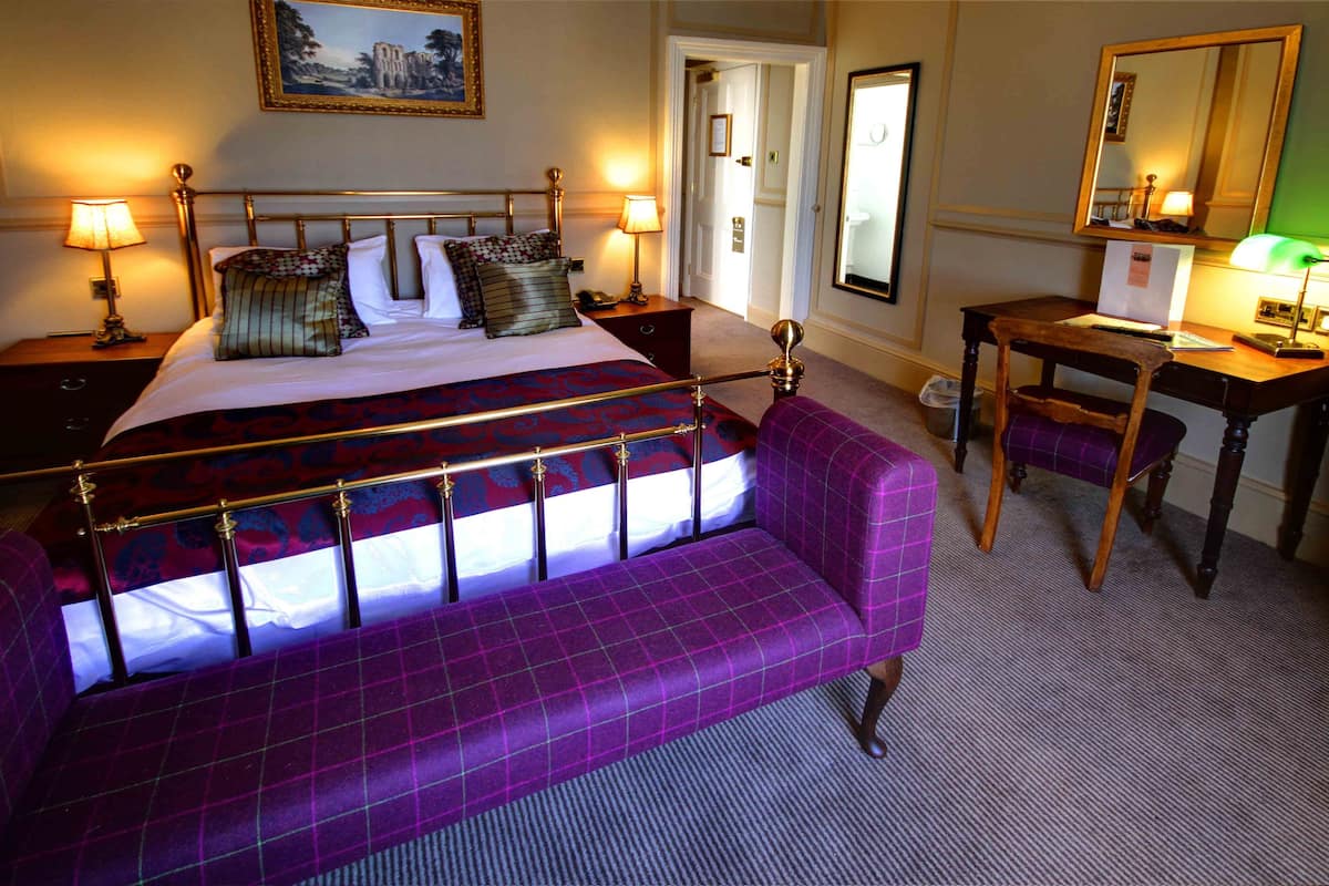 A hotel room with a large bed, a purple sofa, a wooden desk, and two lamps.