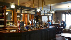 Eine Bar mit Holztresen, Flaschenregalen und hängenden Lampen.