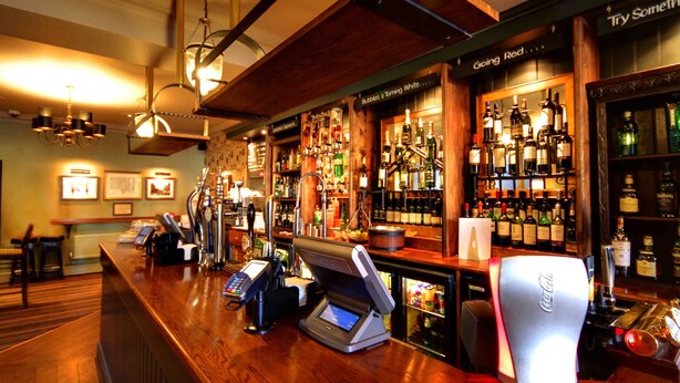 Eine Bar mit Zahlungsterminal, verschiedenen Spirituosenflaschen und einem Schild mit dem Schriftzug 'Try Something Red'.