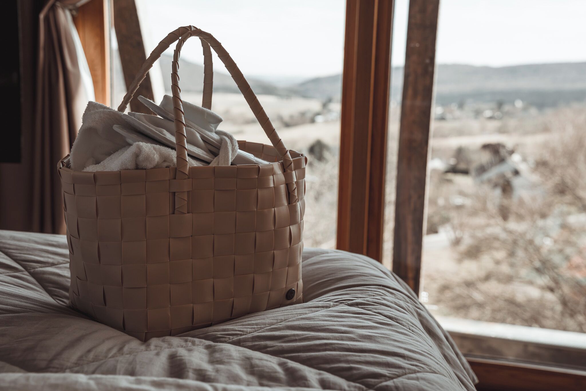 A wicker basket on a bed with a view of a rocky landscape through a window.
