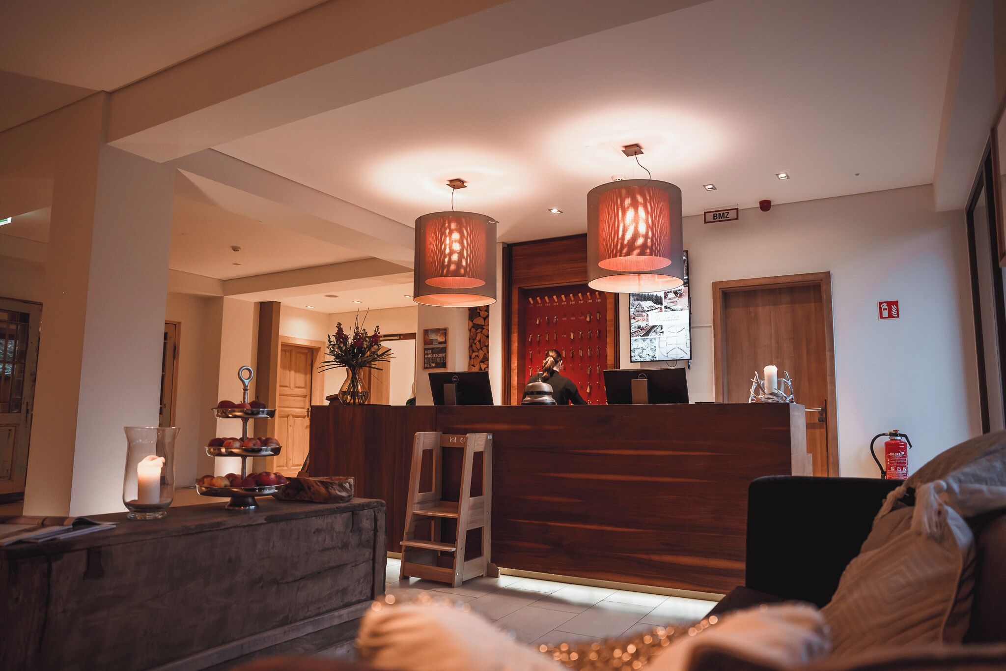 A reception area with a wooden desk, two pendant lights, a vase with a candle, and a fire extinguisher on the wall.