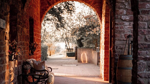 An arched stone doorway leading to a courtyard with a bench and a barrel.
