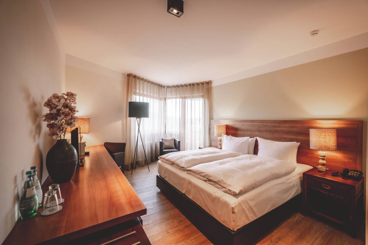 A hotel room with a large bed, bedside tables, a desk, a chair, and a large vase with flowers.
