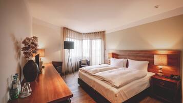 A hotel room with a large bed, bedside tables, a desk, a chair, and a large vase with flowers.
