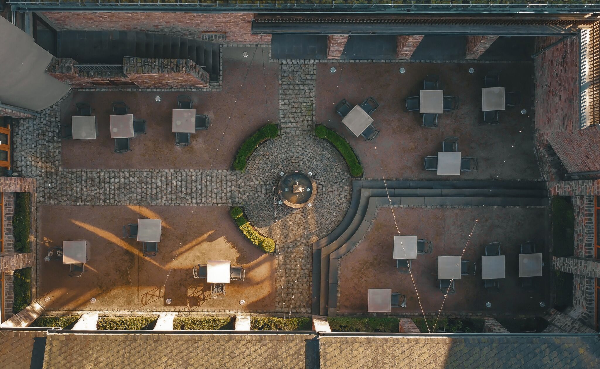 An aerial view of a courtyard with a central fountain, surrounded by seating areas and a brick wall.