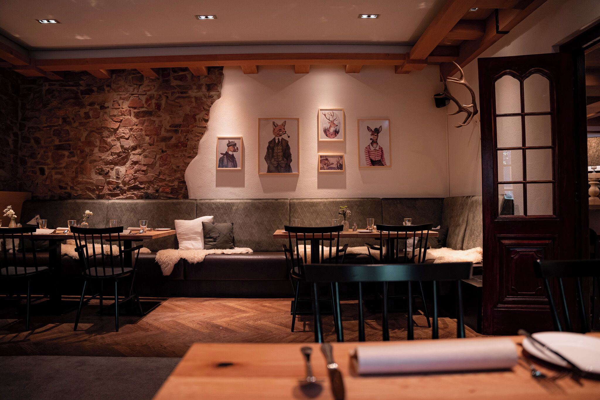 Ein gemütliches Restaurant mit Steinwänden, Holzbalken und einem Kamin aus Stein. Es sind Tische und Stühle zum Essen bereitgestellt, und an den Wänden befinden sich Kunstwerke.