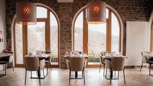 A dining area with wooden tables and chairs, large arched windows, and hanging pendant lights.