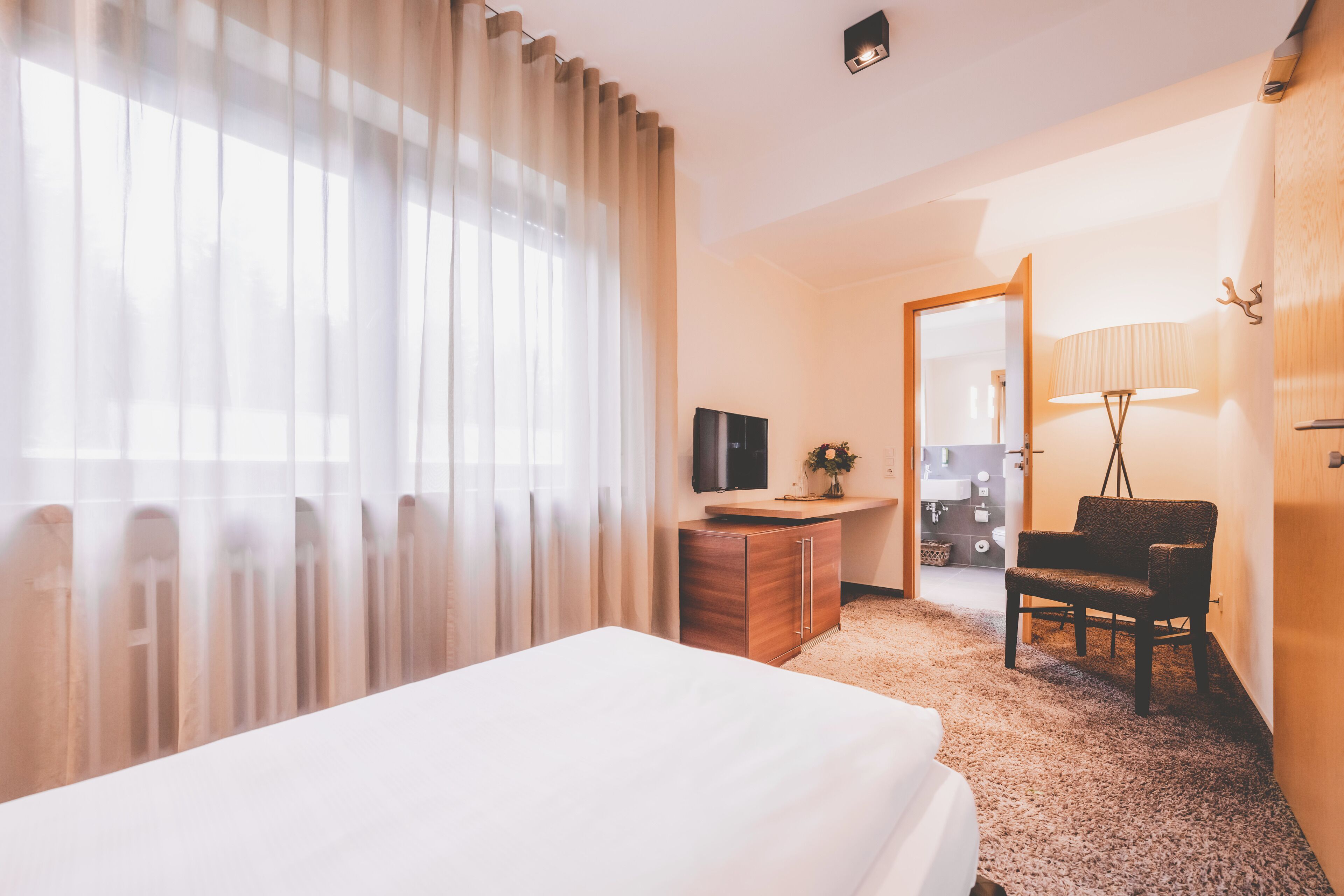 Ein Hotelzimmer mit Bett, Schreibtisch, Stuhl, Fernseher und einem durchgehenden Türbogen einsehbarer Badezimmer.