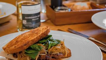 Un sándwich en un plato con un cuchillo y una botella de vino al fondo.