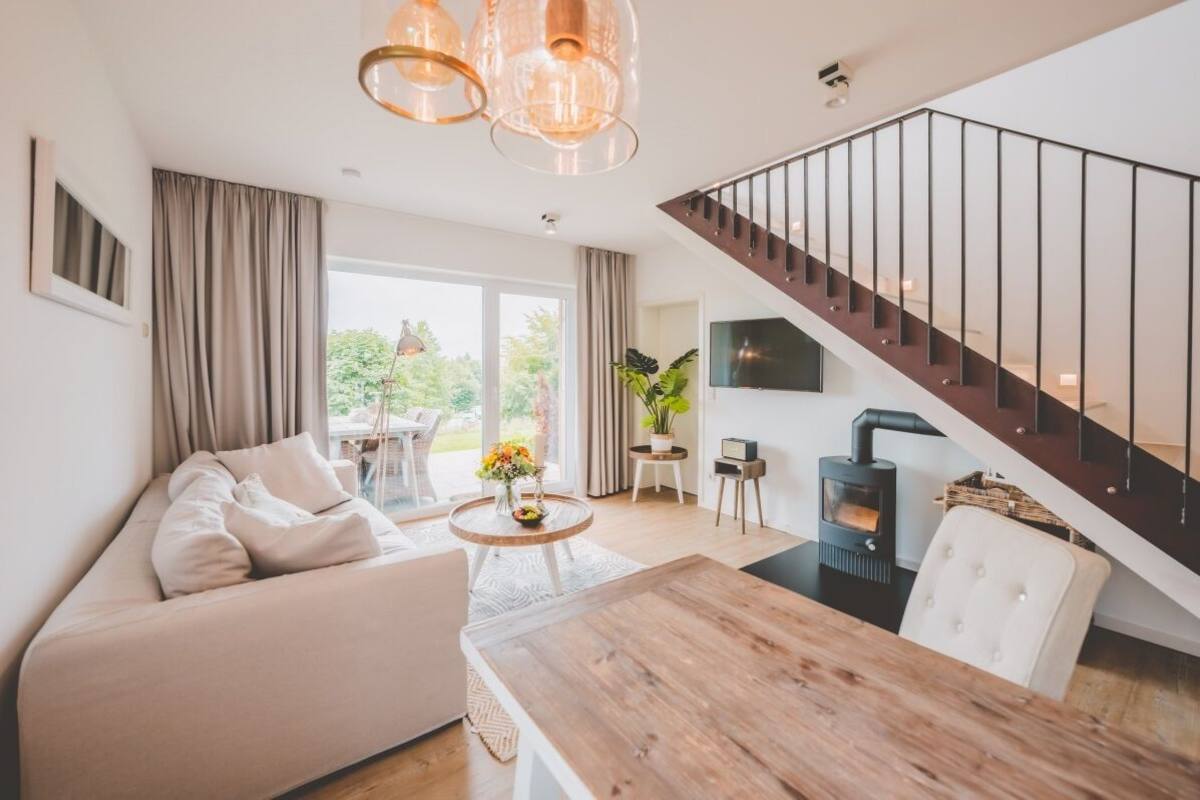 A modern living room with a sofa, a wooden dining table, and a staircase leading to an upper floor.