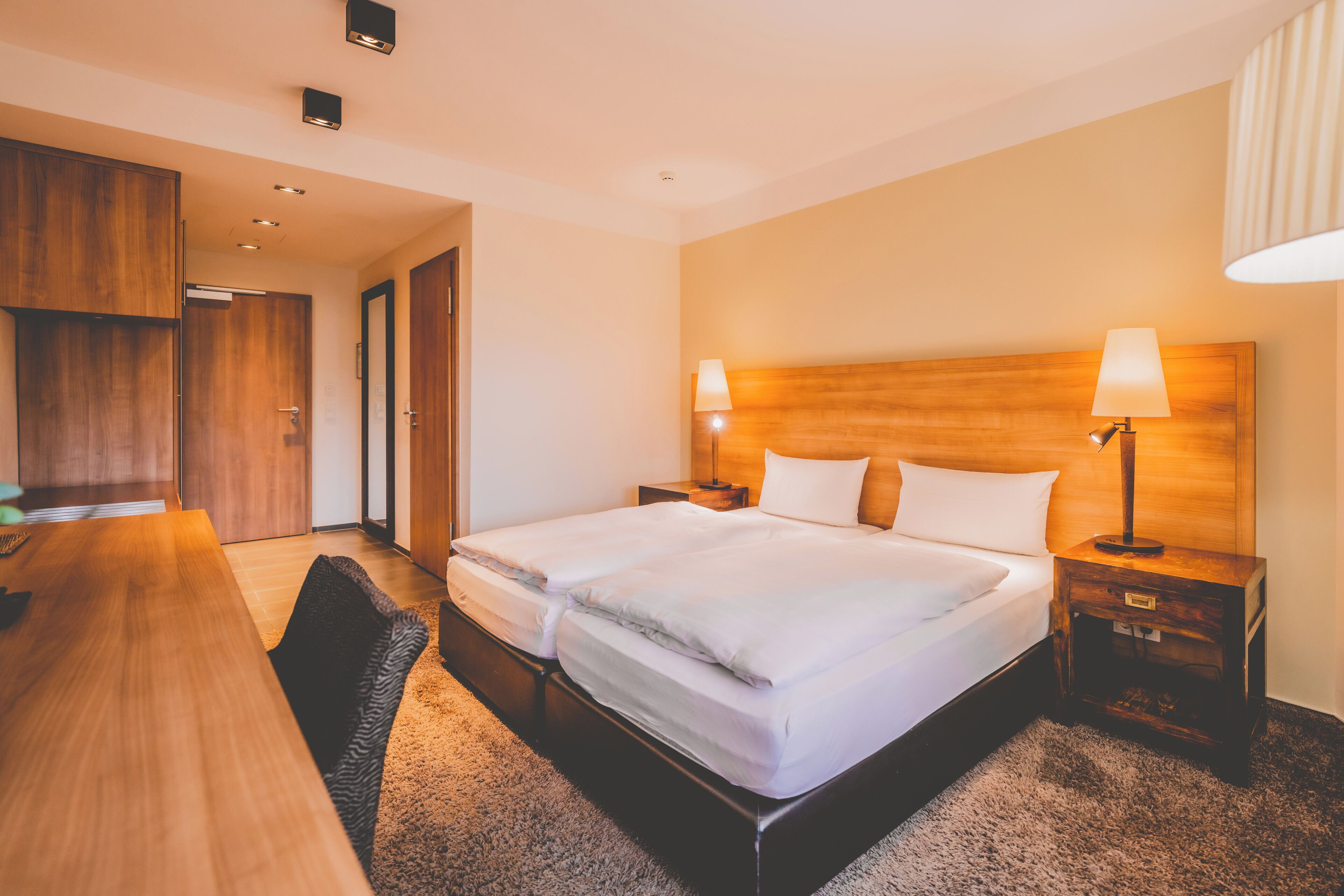Una habitación de hotel con una cama doble, dos mesitas de noche con lámparas, un escritorio de madera y una silla.