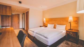 Una habitación de hotel con una cama doble, dos mesitas de noche con lámparas, un escritorio de madera y una silla.