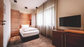 Une chambre d’hôtel avec un lit, une télévision, une armoire en bois et une grande fenêtre avec des rideaux.