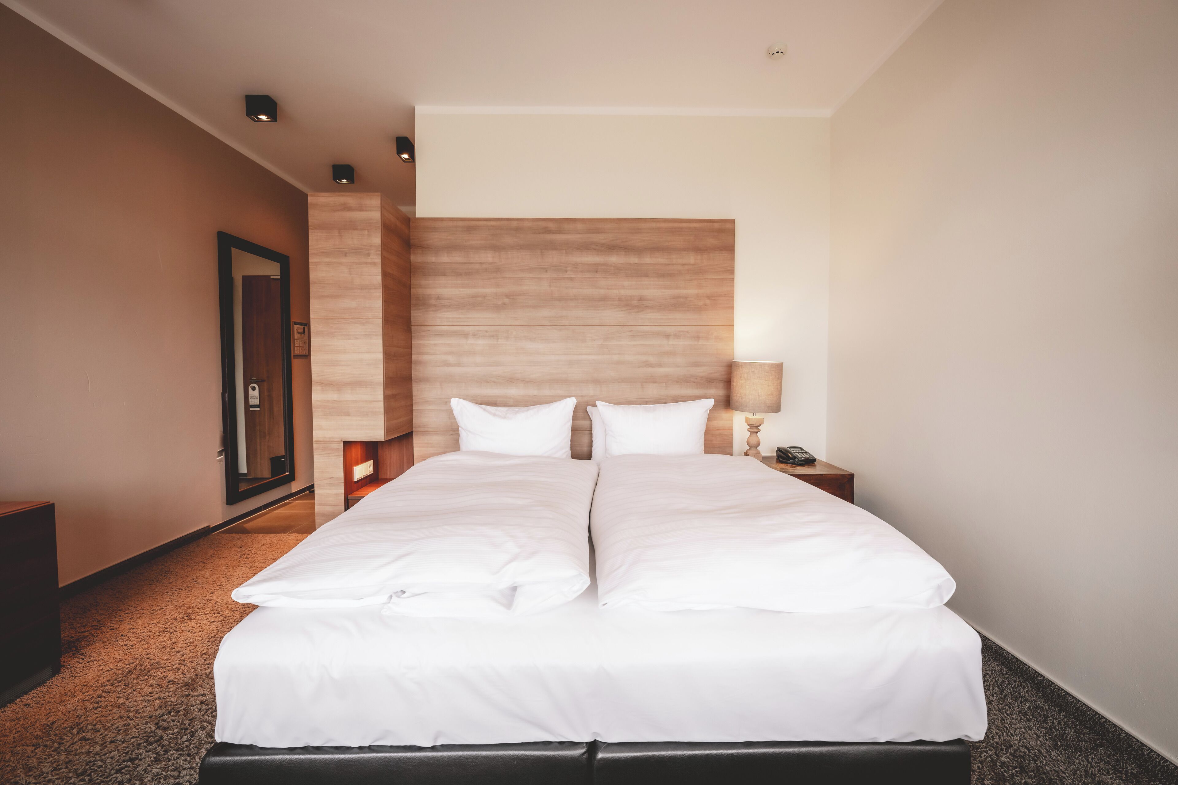 Ein Hotelzimmer mit einem großen Bett, einem Holzkopfende, einem Nachttisch mit einer Lampe und einem Beistelltisch mit einem Telefon.