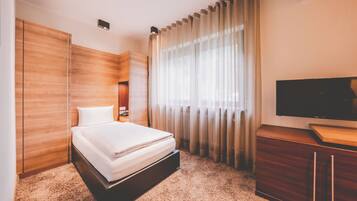 A hotel room with a bed, wooden wardrobe, a TV, and a large window with curtains.